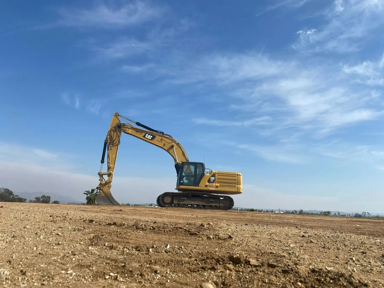 Cat excavator on a wide, freshly graded dirt field under a blue sky