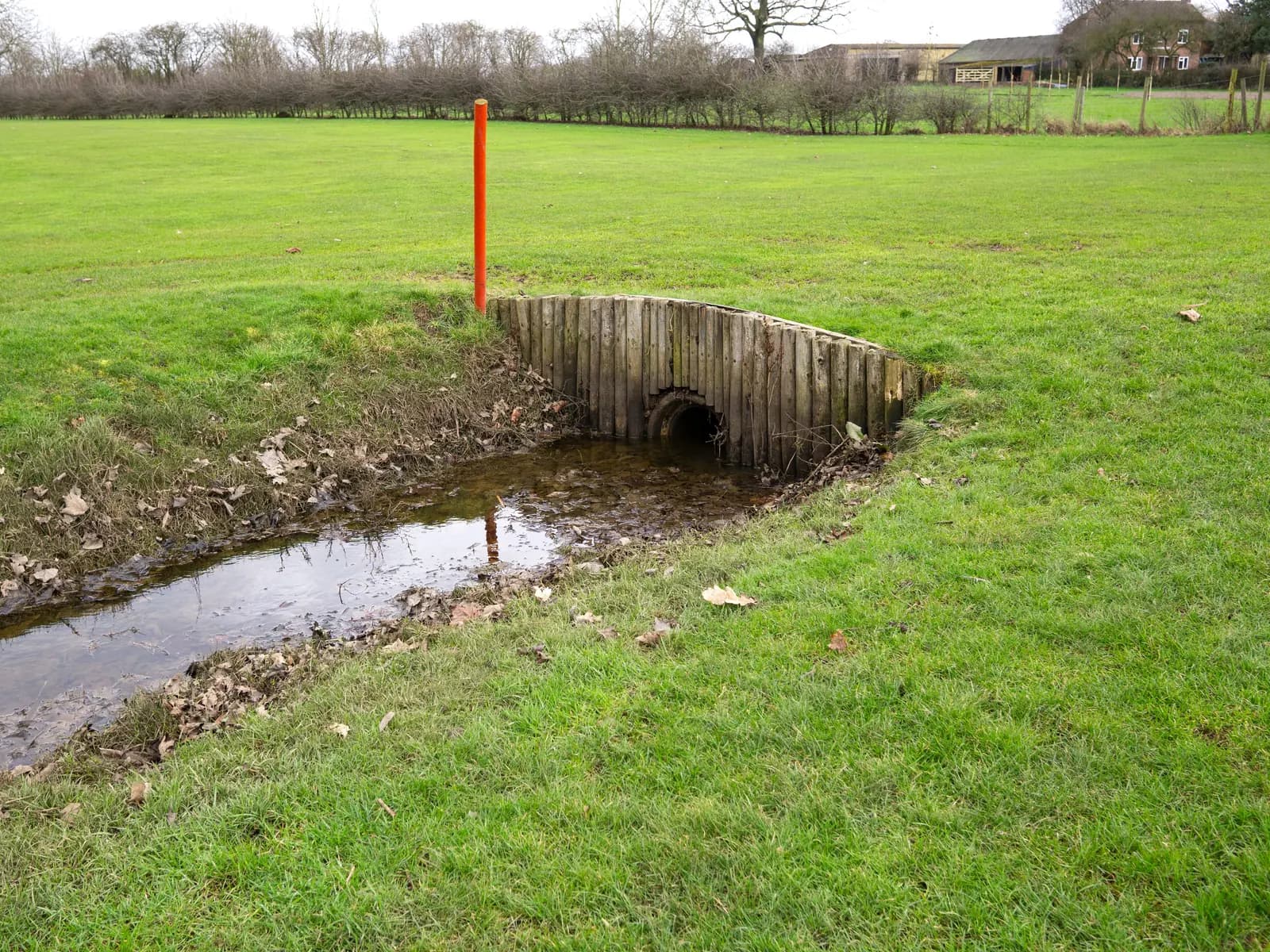 Timber culvert crossing over a drainage ditch in a grassy field