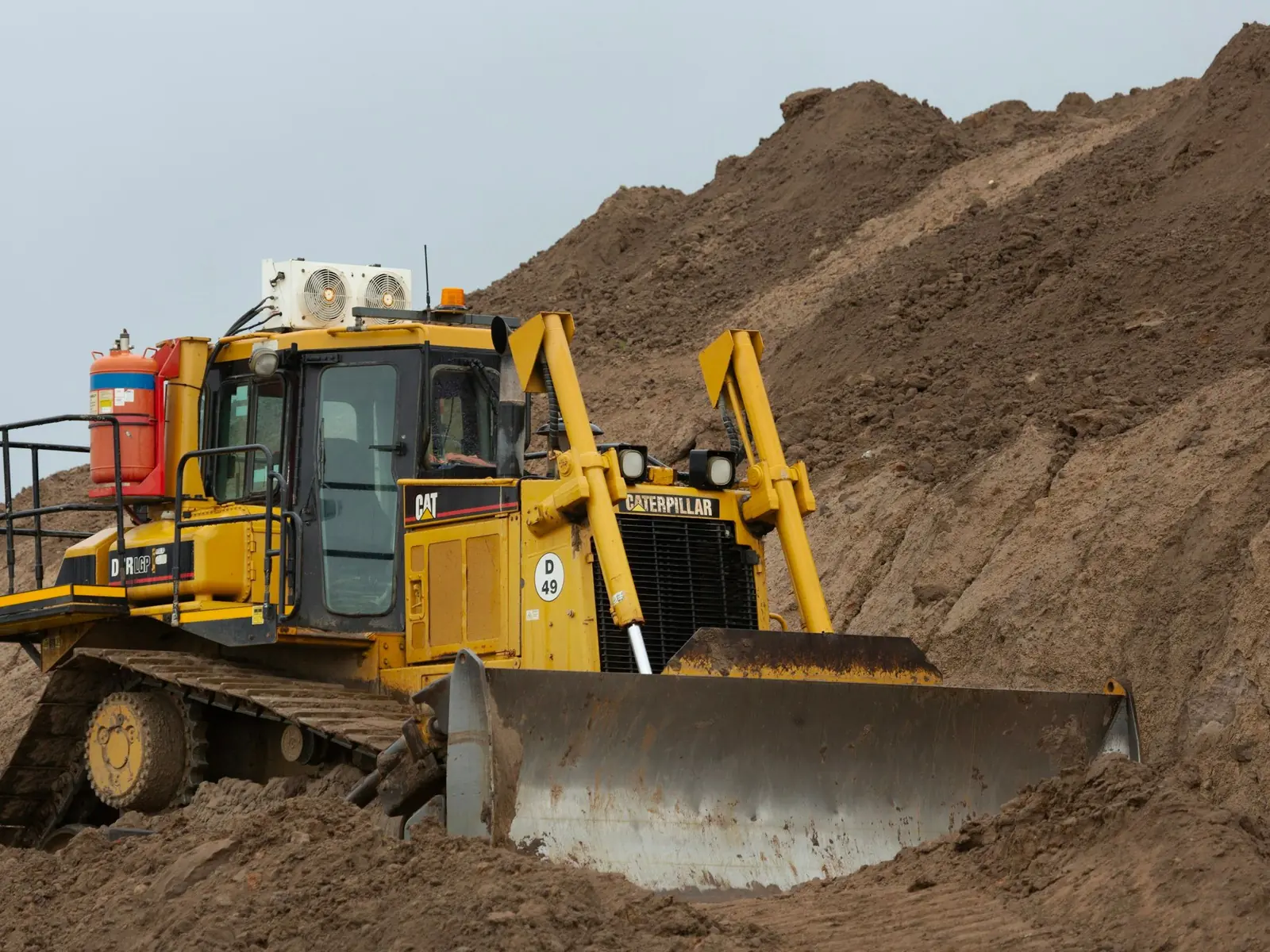 Cat bulldozer pushing a load of brown earth while grading a route