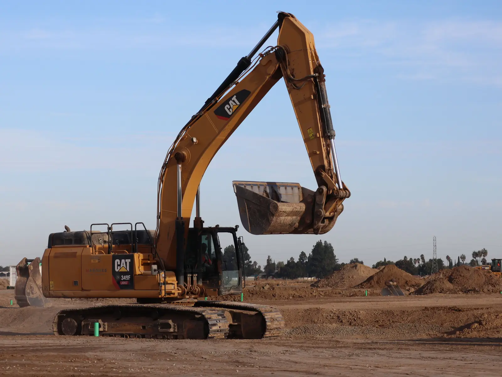 Cat excavator with its bucket raised on a large graded dirt site