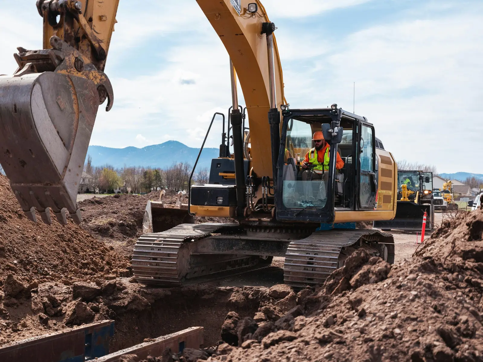 Operator digging with a Cat excavator on an excavation site with hills behind