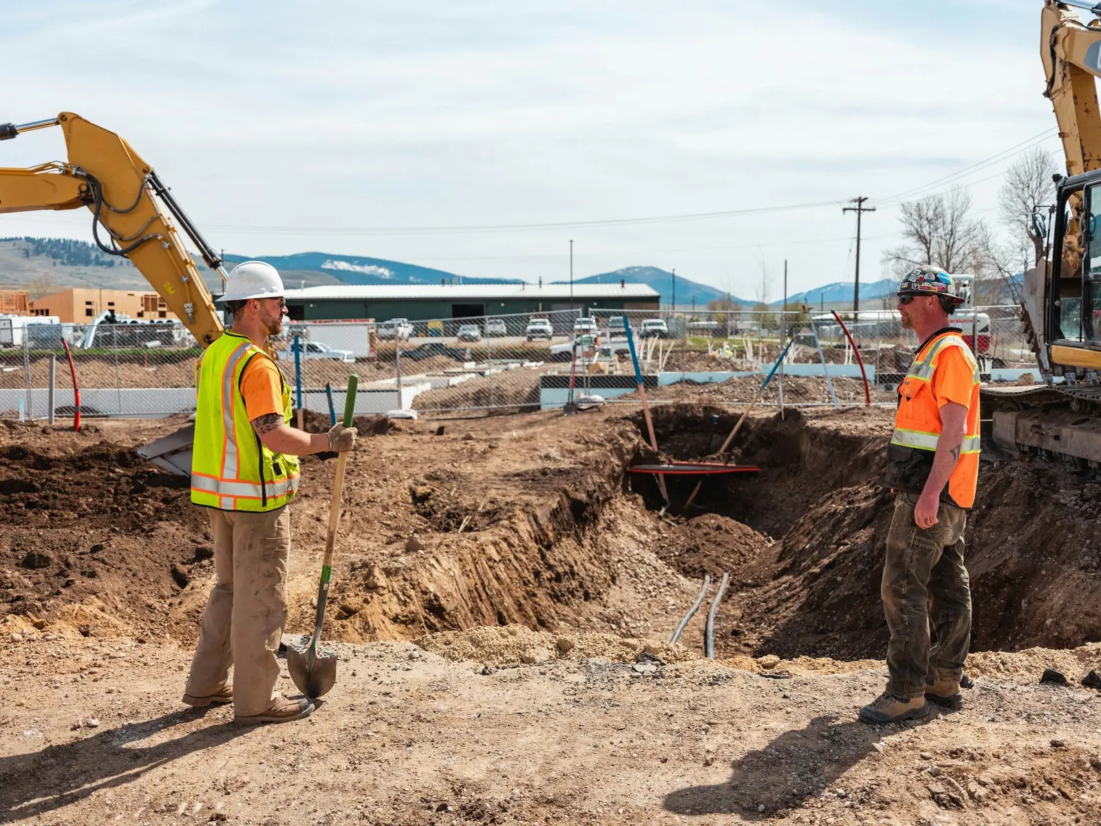 Crew checking a fresh excavation while a Cat excavator works the edge of the pit