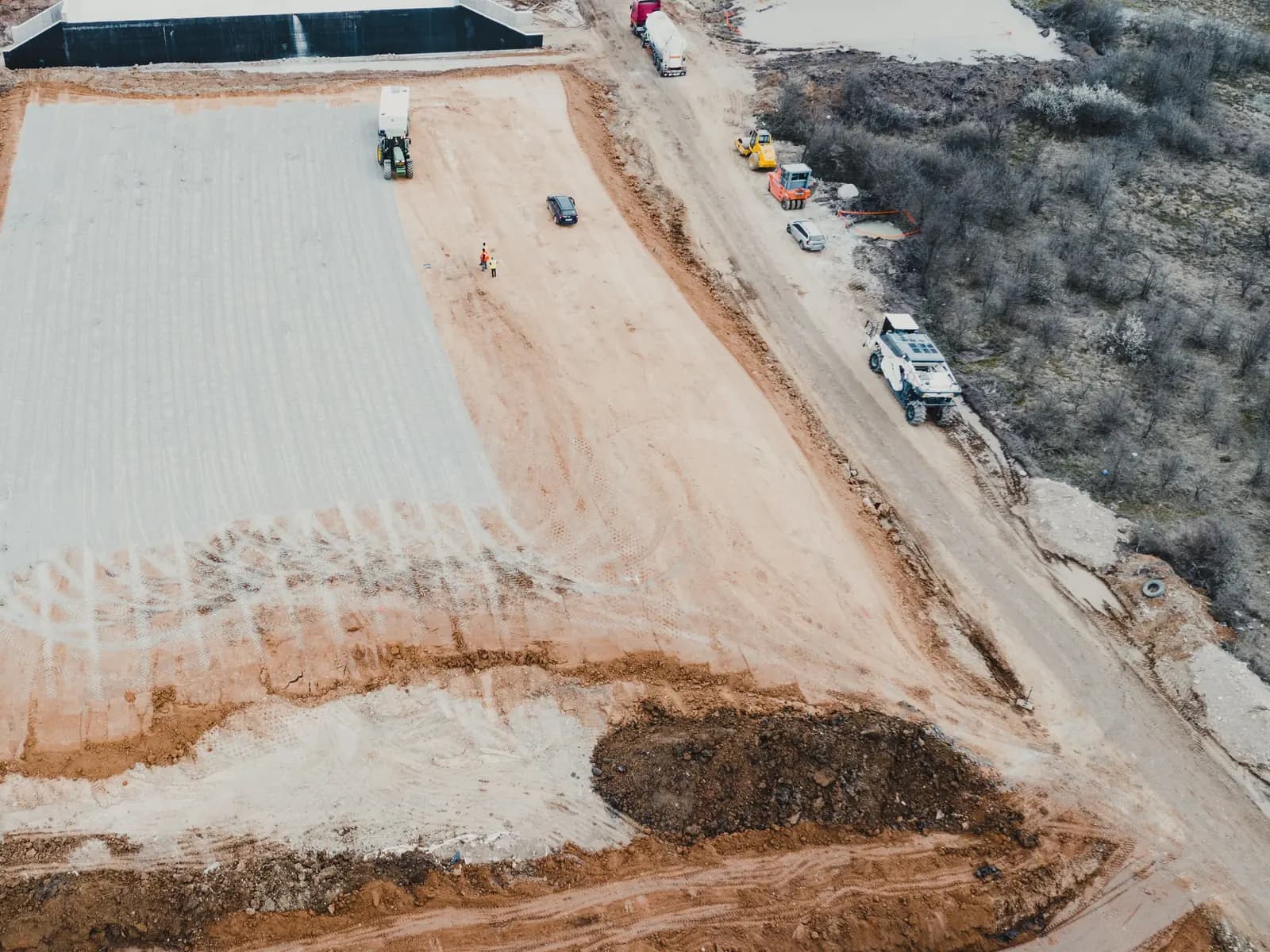 Aerial view of a graded building pad with trucks and a dozer along the edge
