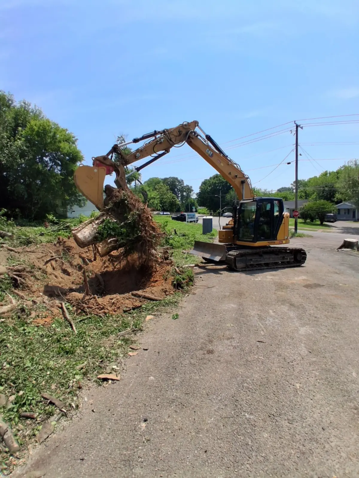 Excavator thumb pulling a large stump from a cleared lot next to a paved street, by Superior Land Management