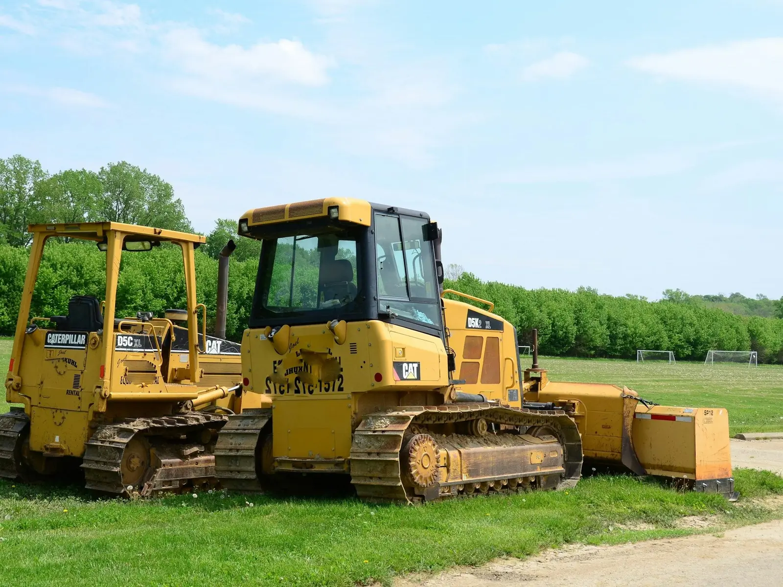 Two Cat dozers parked on a grass field beside a tree line