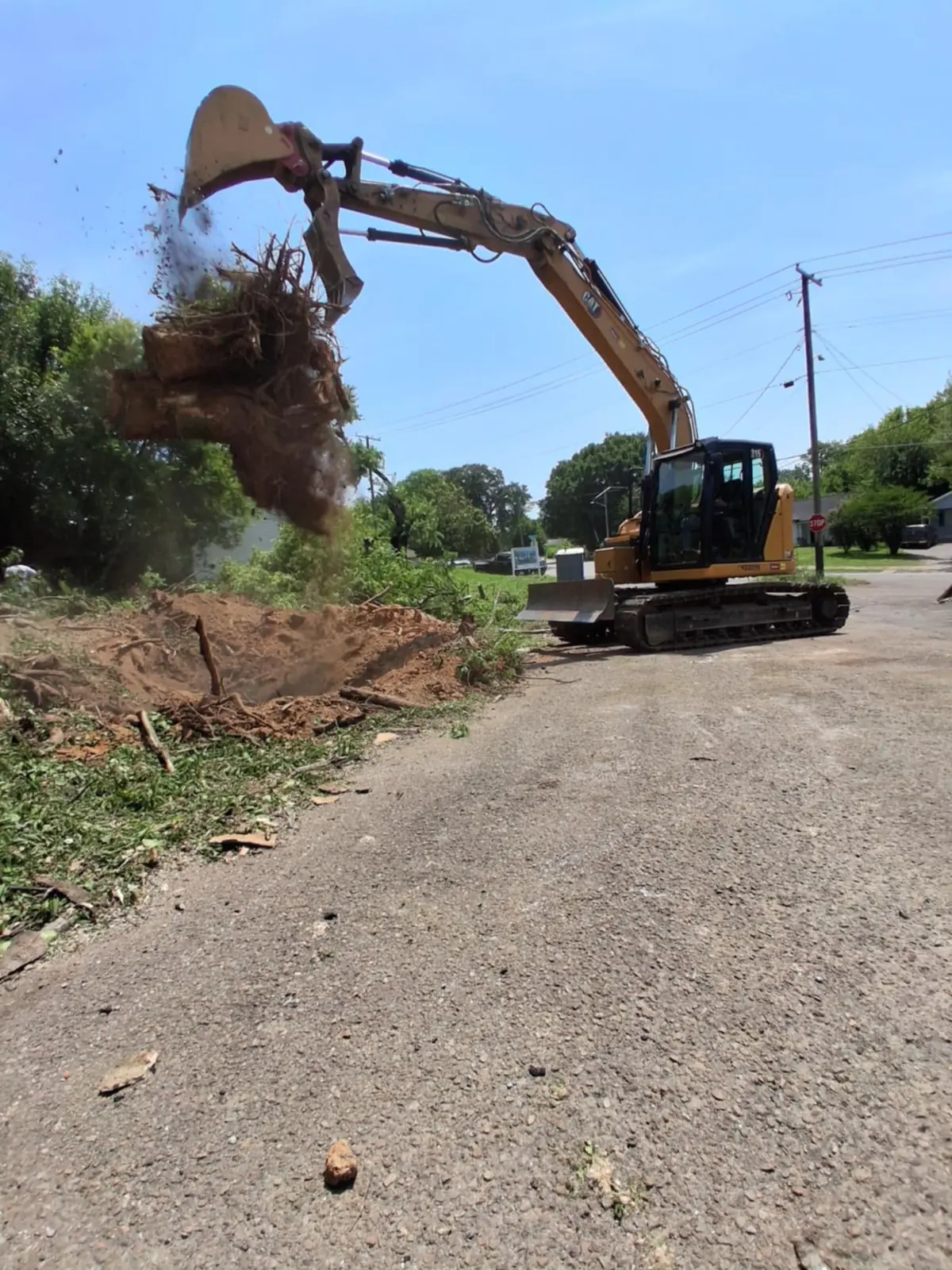 Cat excavator lifting a stump and root ball out of the ground during lot clearing by Superior Land Management